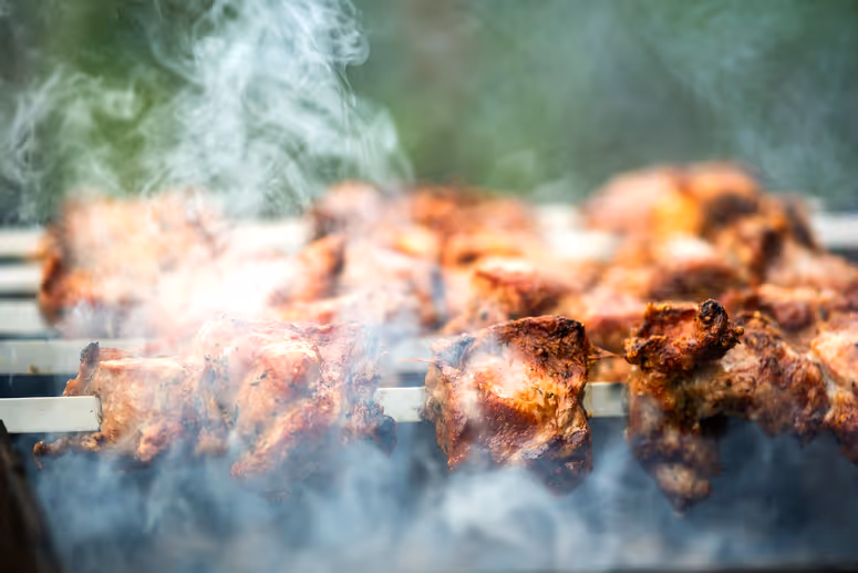 Marinated meat pieces grilling on skewers over a smoky barbecue.
